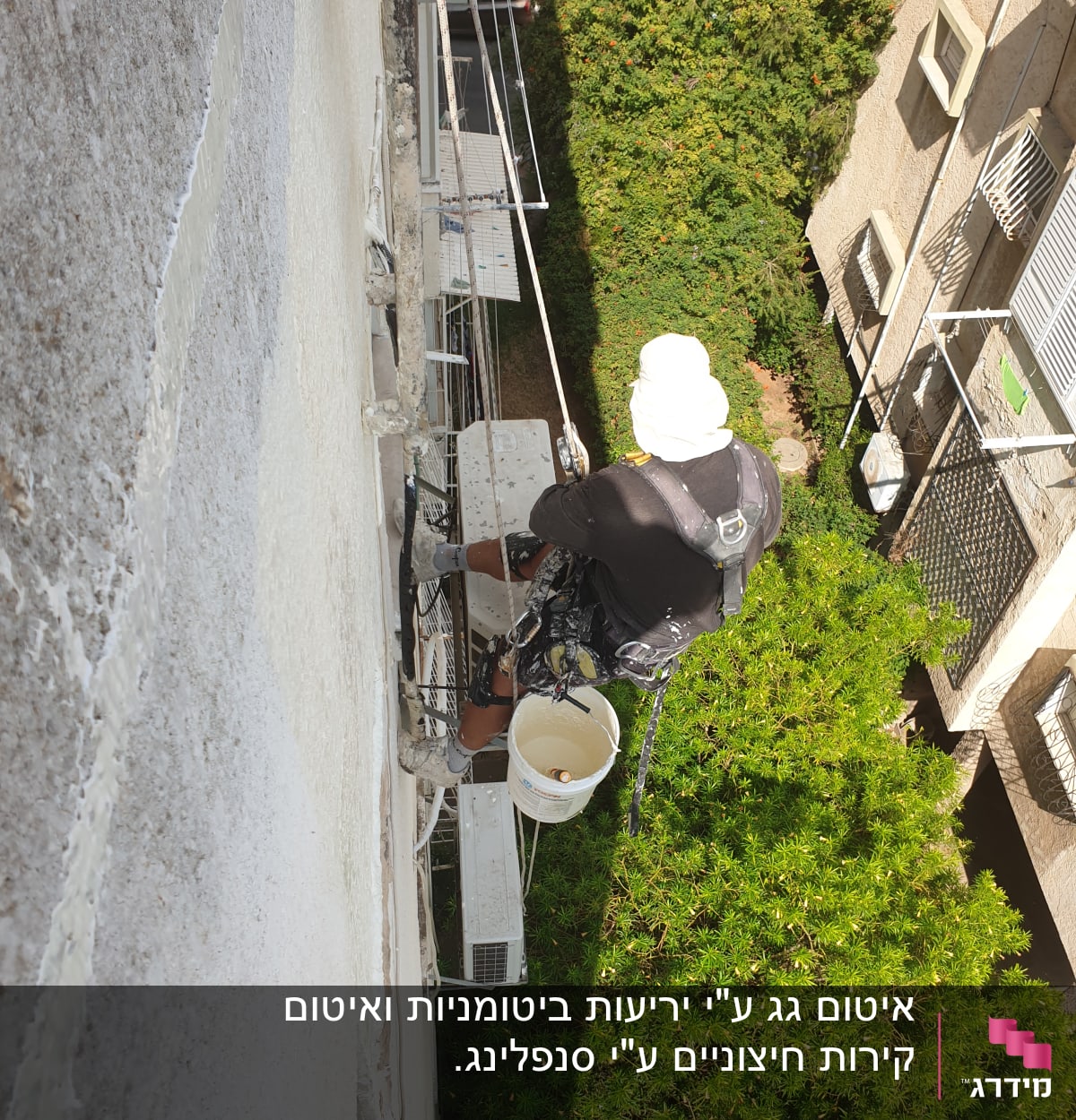 אדם על פיגום עם דלי צבע אוטם קיר חיצוני